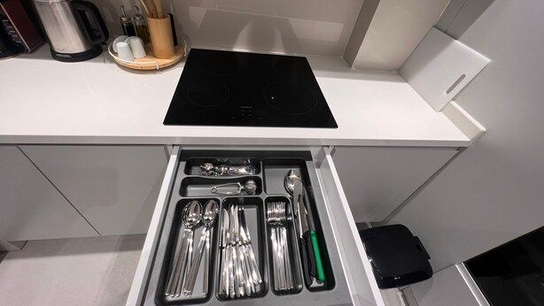 Una cocina con estufa integrada, cafetera y utensilios en un cajón.
