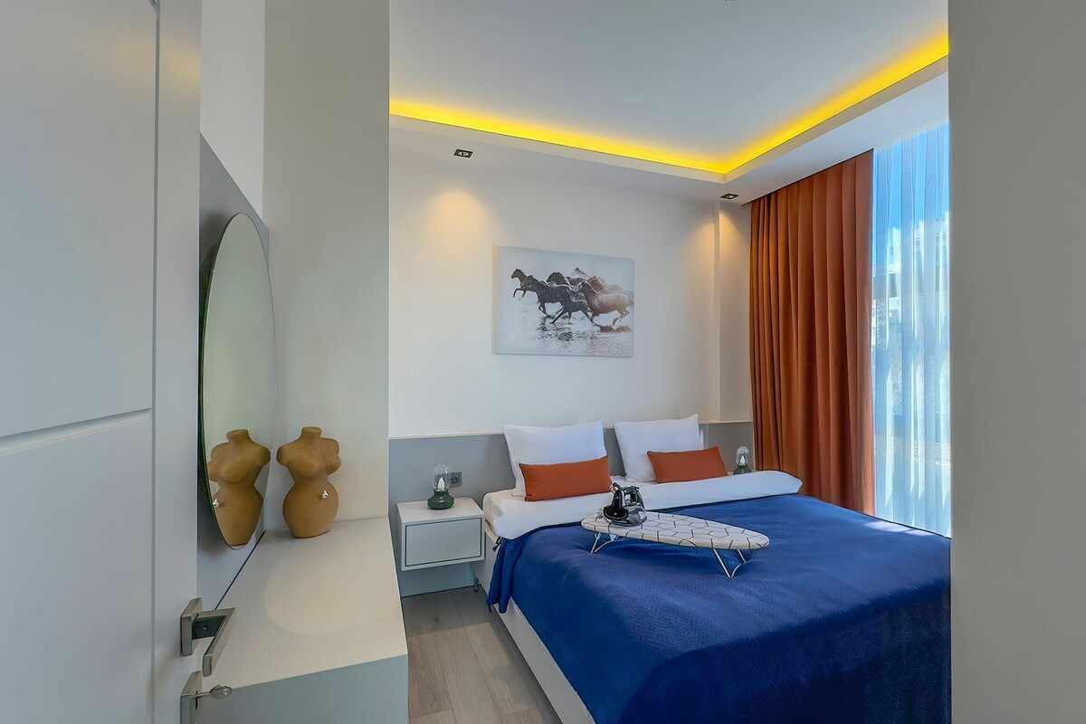 A modern hotel room with a large bed, a bedside table, a nightstand, and a wall-mounted mirror.