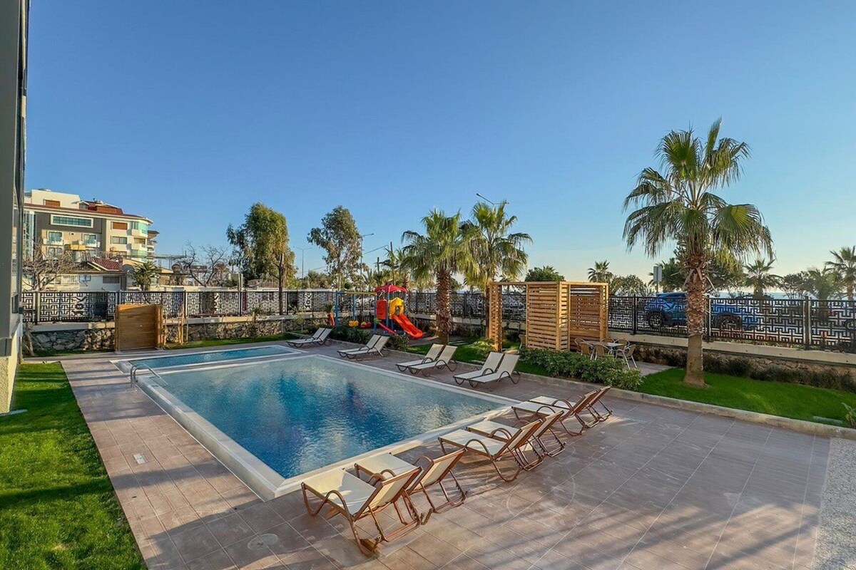 A swimming pool with lounge chairs, palm trees, and a slide.