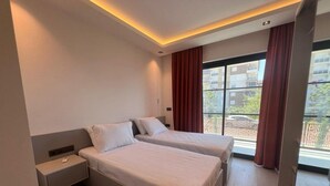 Ein modernes Hotelzimmer mit zwei Betten, einem Nachttisch und einem großen Fenster mit Vorhängen.