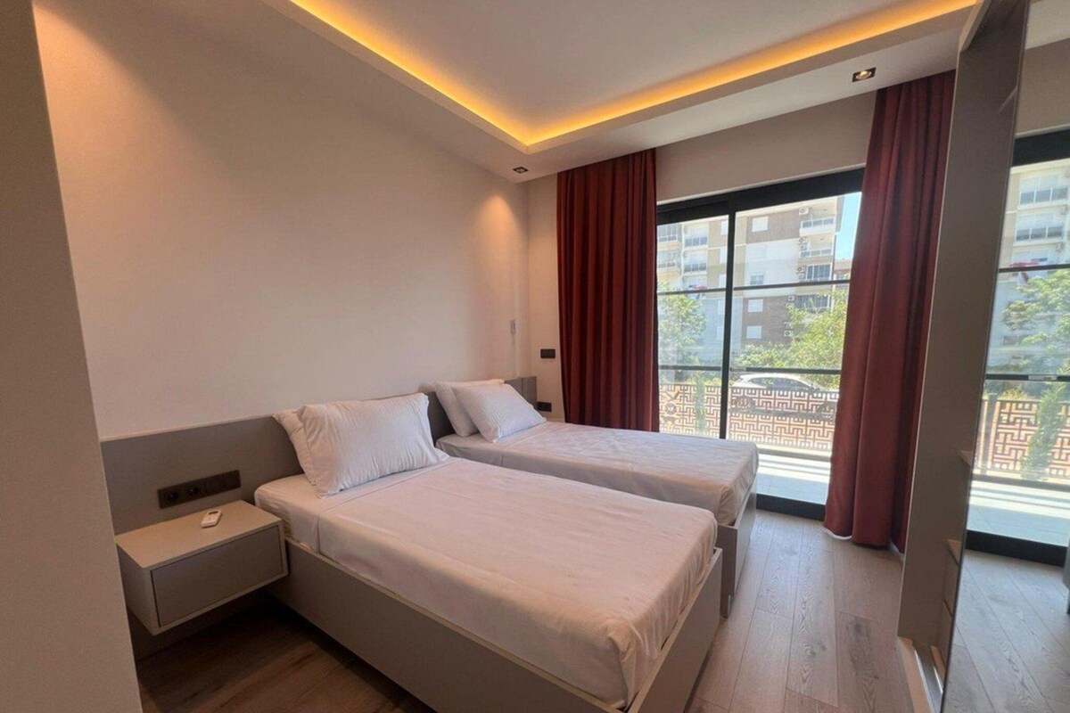 Ein modernes Hotelzimmer mit zwei Betten, einem Nachttisch und einem großen Fenster mit Vorhängen.