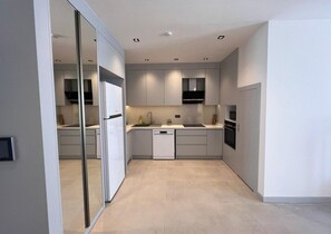 A modern kitchen with white cabinets, a dishwasher, a stove, and a microwave. - Ulu Residence Alanya (Alanya)