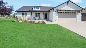 Ein eingeschossiges Haus mit Garage, einer Veranda mit zwei Stühlen und einem gepflegten Rasen.