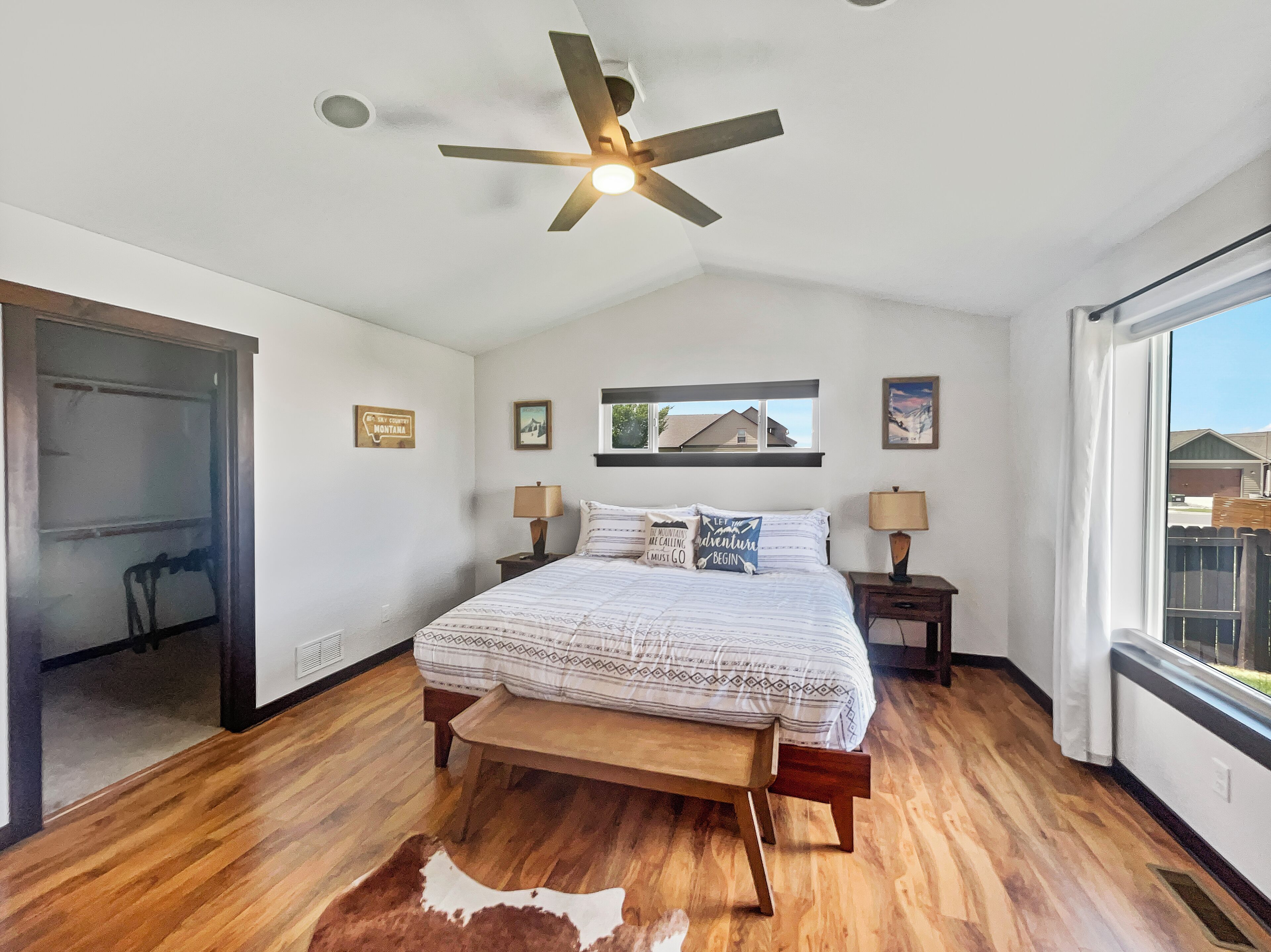A bedroom with a bed, bedside tables, a ceiling fan, a window, and a door.