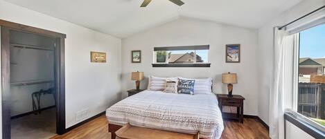 A bedroom with a bed, bedside tables, a ceiling fan, a window, and a door.