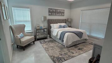 A bedroom with a bed, a chair, a nightstand, a ceiling fan, and a window with blinds.