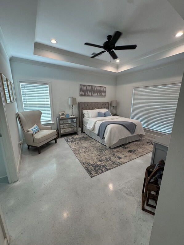 A bedroom with a bed, a chair, a nightstand, a ceiling fan, and a window with blinds.