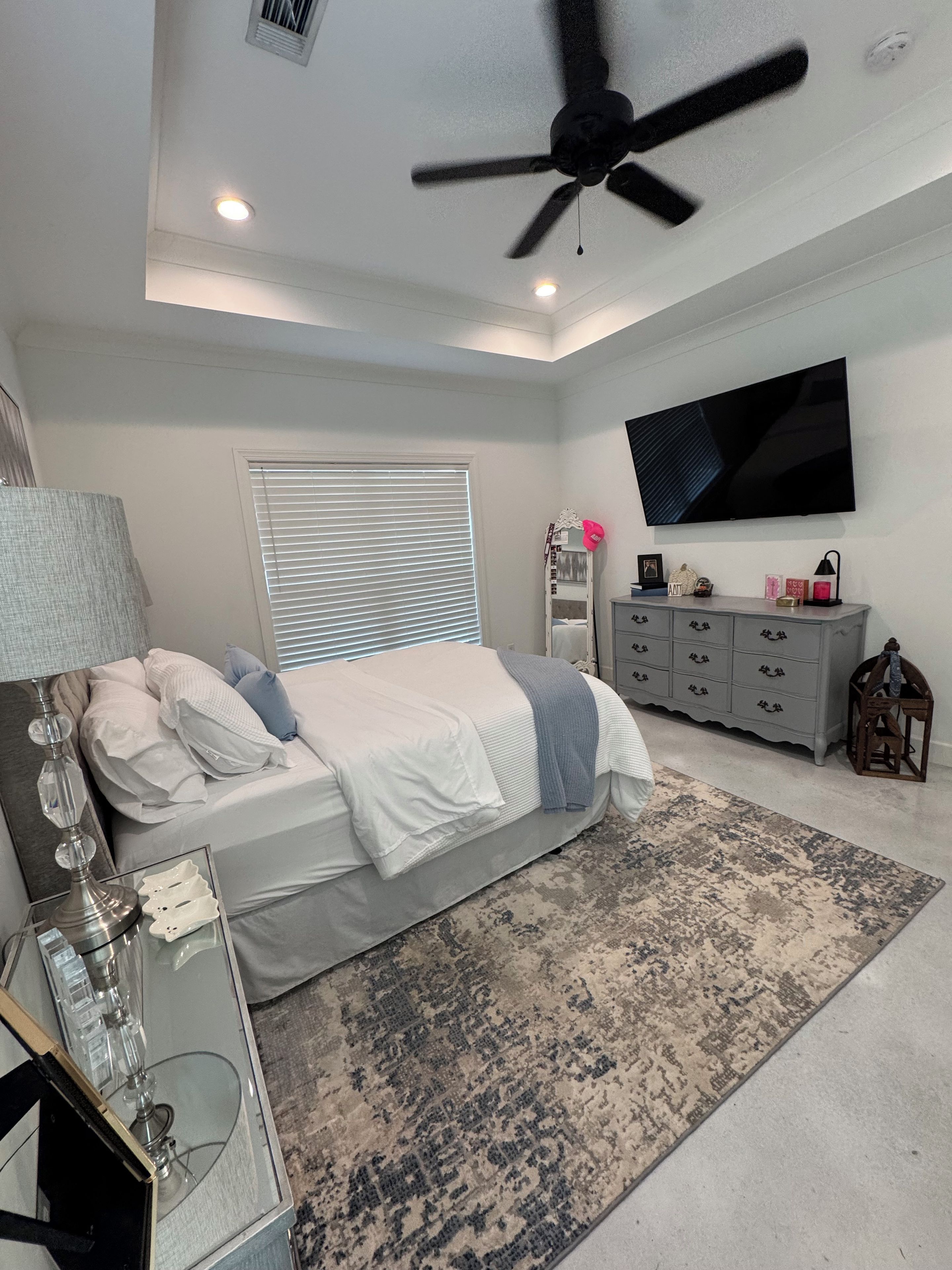 A bedroom with a bed, a ceiling fan, a TV, a dresser, and a bedside table.