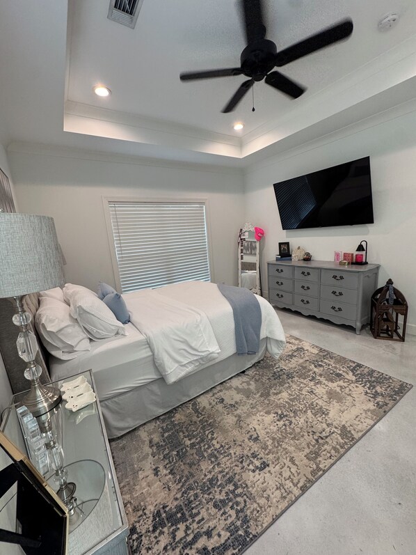 A bedroom with a bed, a ceiling fan, a TV, a dresser, and a bedside table.