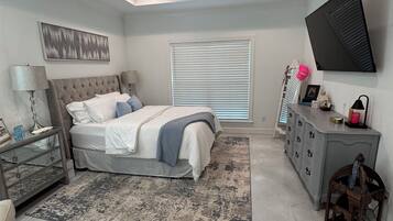 Ein Schlafzimmer mit einem Bett, einem Deckenventilator, einem Fernseher, einem Fenster mit Jalousien und einer Kommode.