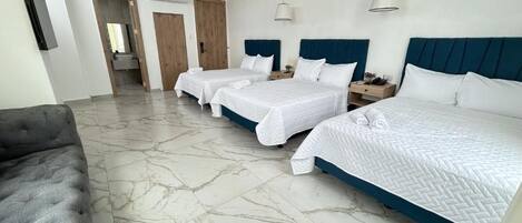 A hotel room with three beds, a grey sofa, and a marble floor.
