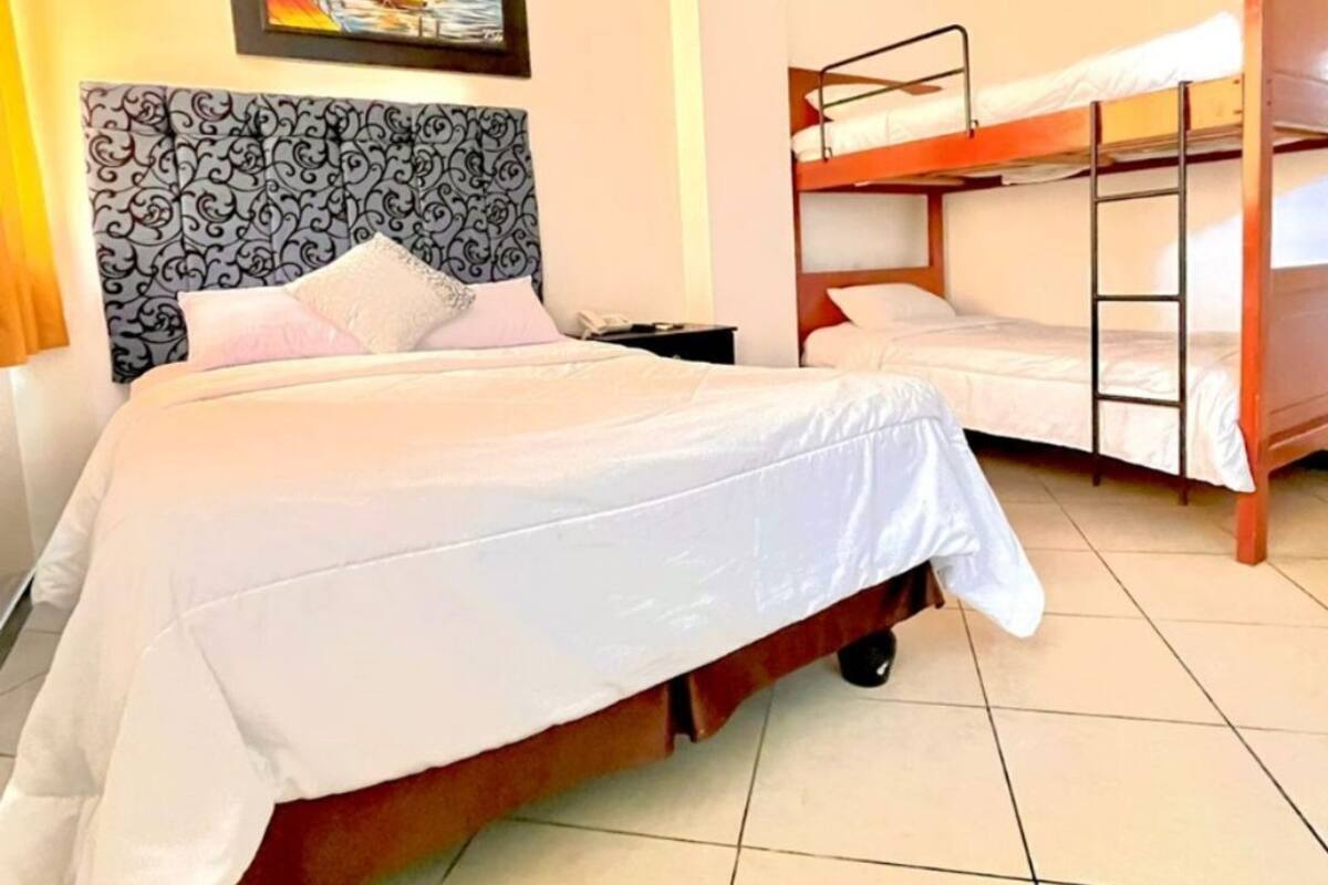 Quarto de hotel com uma cama grande, uma cama menor, uma beliche e um quadro na parede.