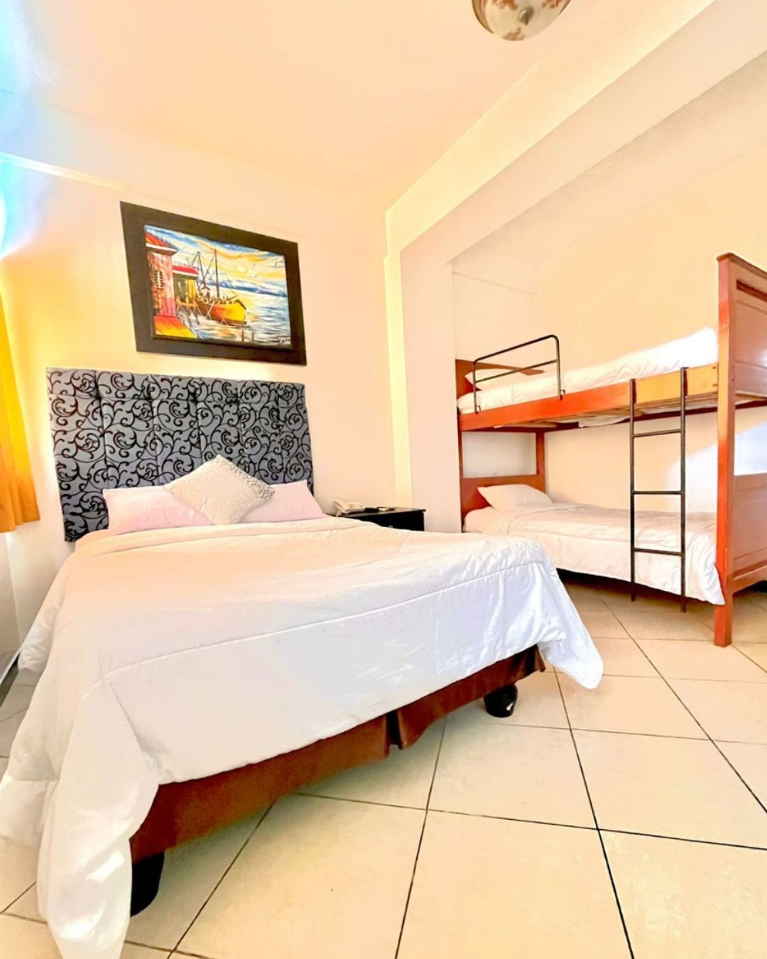Ein Hotelzimmer mit einem großen Bett, einem kleineren Bett, einem Etagenbett und einem Bild an der Wand.