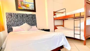 Ein Hotelzimmer mit einem großen Bett, einem kleineren Bett, einem Etagenbett und einem Bild an der Wand.