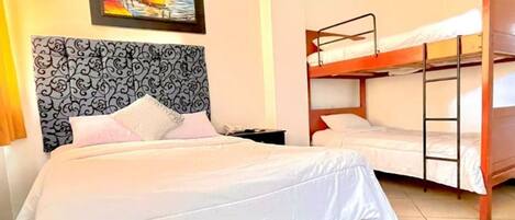 A hotel room with a large bed, a smaller bed, a bunk bed, and a painting on the wall.