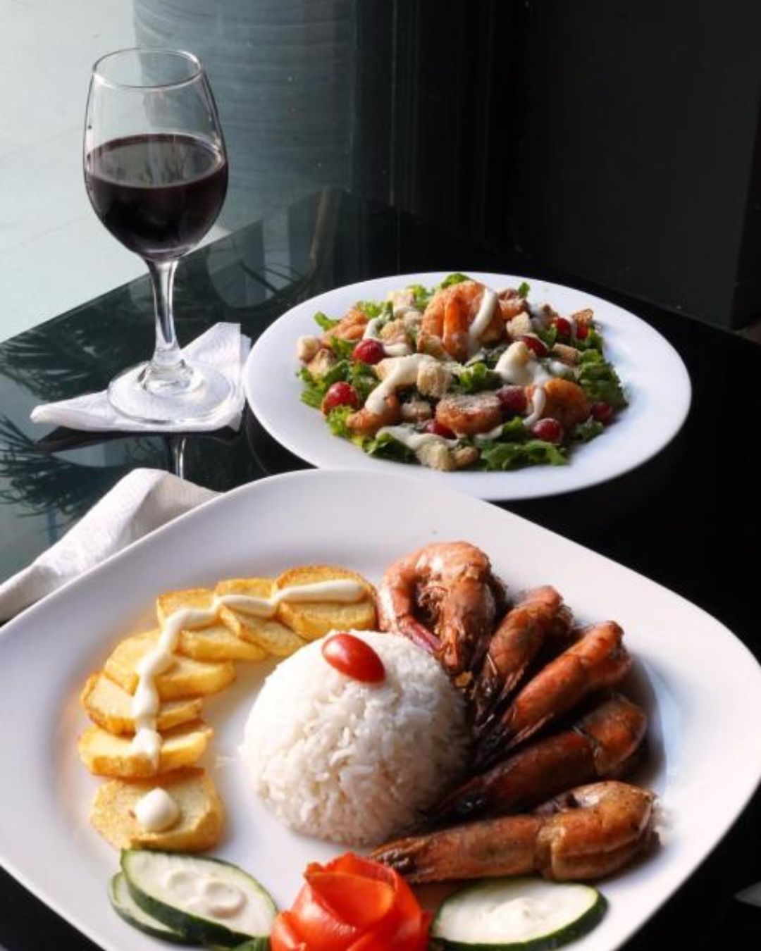 Two plates of food on a table with a glass of red wine.