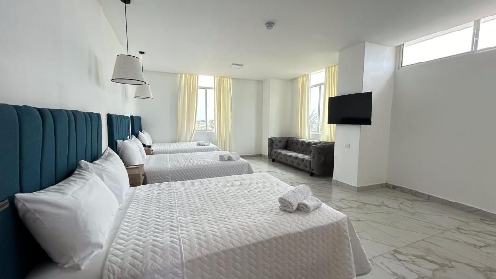 A hotel room with two beds, a sofa, a flat-screen TV, and large windows with curtains.