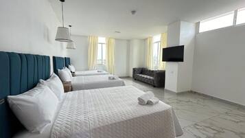 A hotel room with two beds, a sofa, a flat-screen TV, and large windows with curtains.