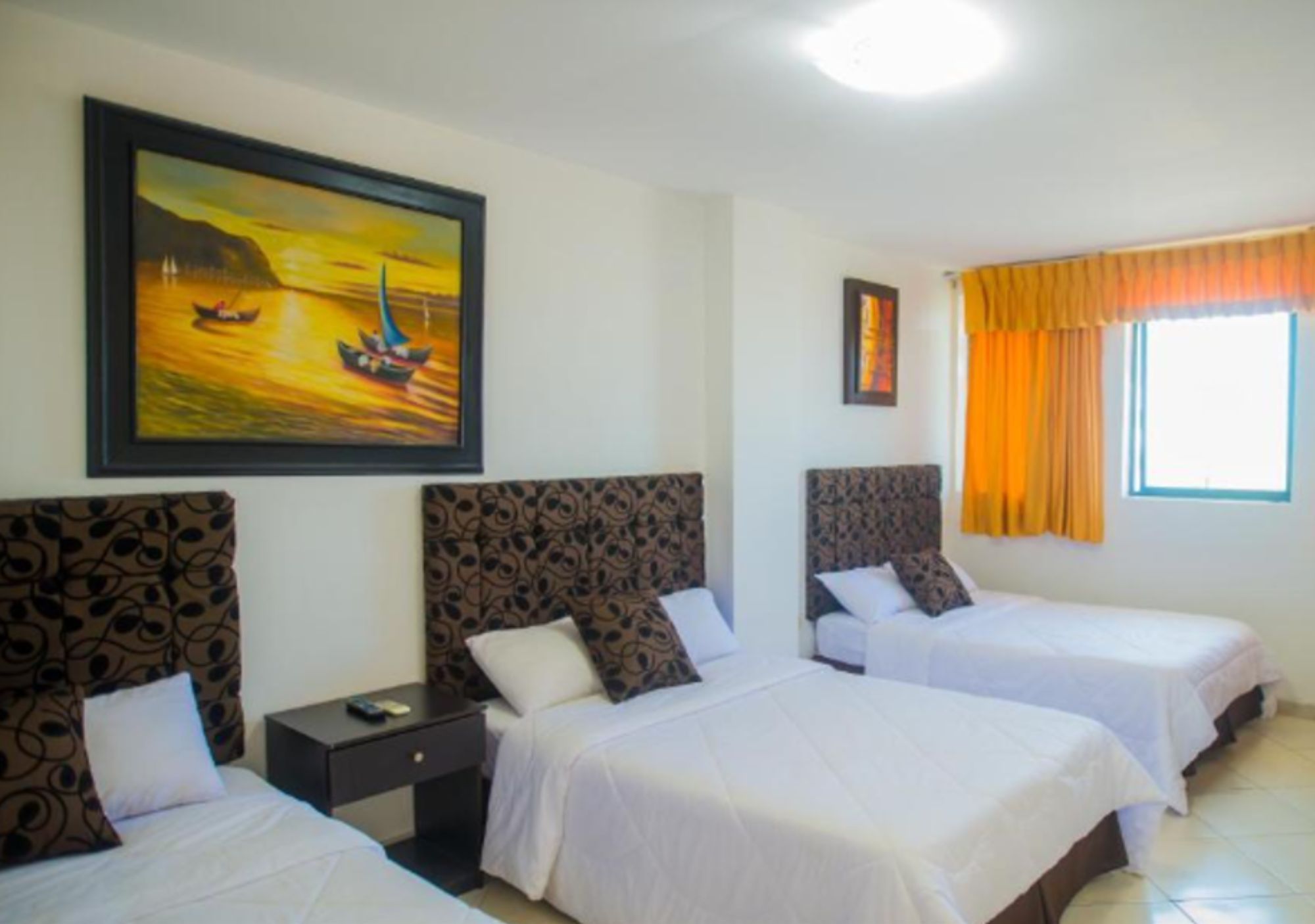 A hotel room with two beds, a nightstand, a painting of a sunset over water, and a window with curtains.