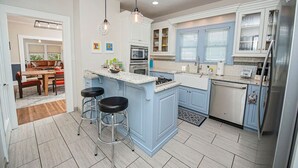 Et moderne køkken med en central ø, barstole, spiseplads med sofa og bord samt et køleskab.