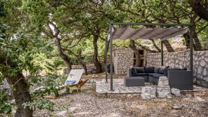 Un espace extérieur aménagé, abrité et doté d’un mur en pierre servant de décor, d’un canapé confortable et d’un fauteuil de jardin à rayures.
