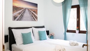 Une chambre d’hôtel bien rangée, avec un lit, des oreillers, une table de chevet, une lampe, un vase avec des fleurs et une fenêtre avec des rideaux.