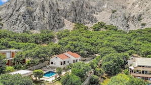 Une villa dotée d’une piscine, entourée d’une végétation luxuriante et adossée à une montagne rocheuse.