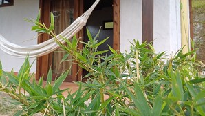A hammock tied between wooden beams under a roofed structure, with a view of a building entrance and surrounding greenery. - Cozy cabin in charming Jardin with WiFi (Jardin)
