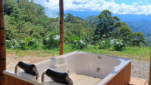 A hot tub under a bamboo structure with a scenic view of a lush landscape. - Cozy cabin in charming Jardin with WiFi (Jardin)