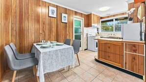 A compact kitchen with wooden cabinets, a dining table with chairs, and a refrigerator. - Retro Retreat - Mornington (Mornington)