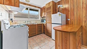 A compact kitchen with wooden cabinets, a gas stove, a microwave, and a refrigerator. - Retro Retreat - Mornington (Mornington)