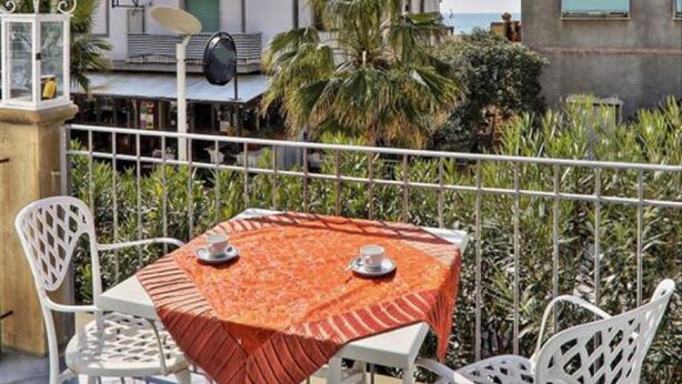 Un balcon avec une table et des chaises, une vue sur la mer et un bâtiment en arrière-plan.