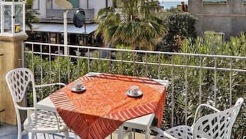 Un balcone con tavolo e sedie, un corrimano e vista su edifici e vegetazione.