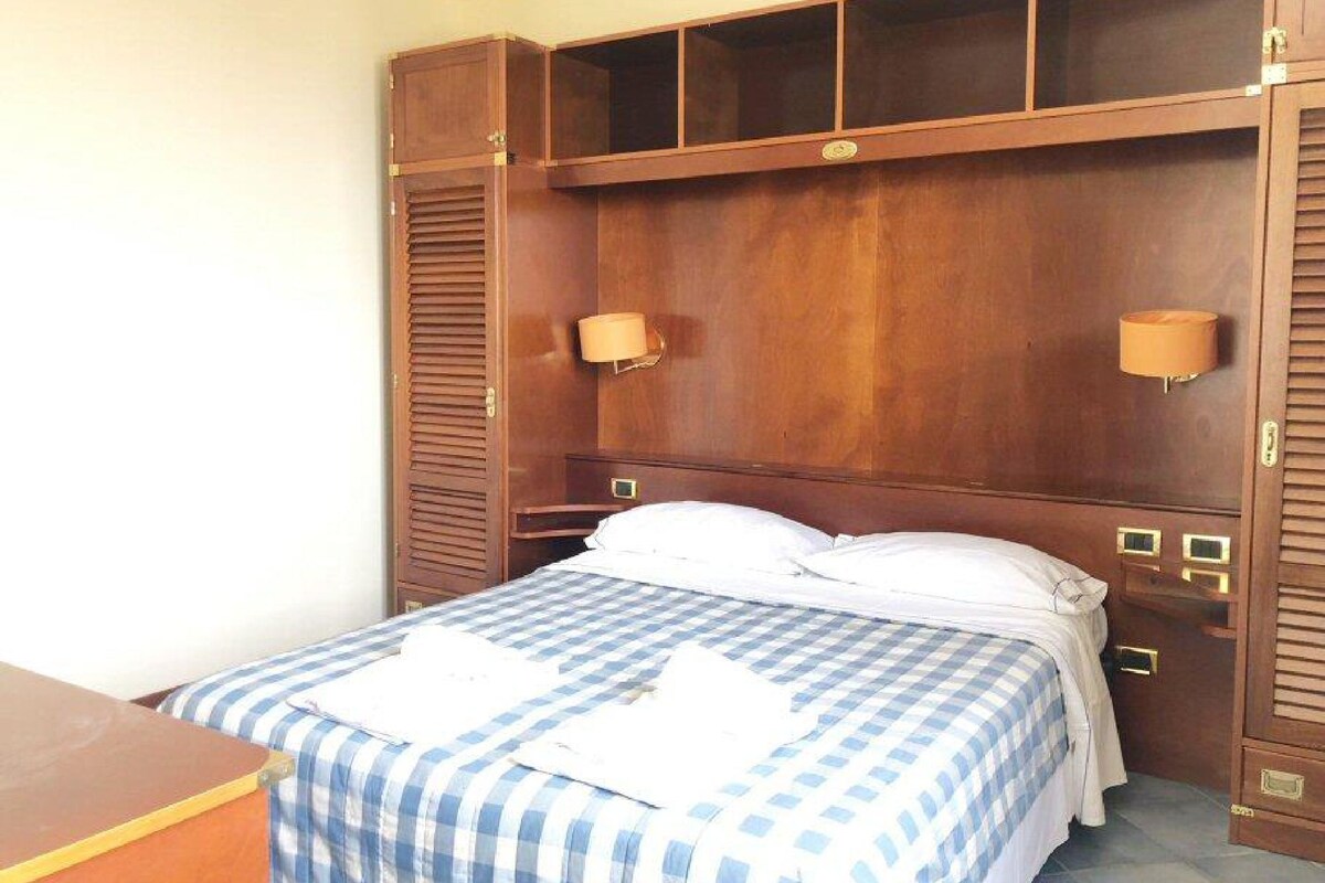 A hotel room with a large bed, a wooden wardrobe with multiple compartments, and two wall-mounted lamps.