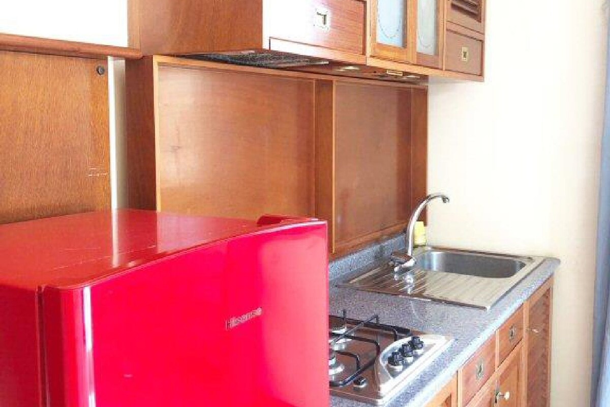 A compact kitchen with wooden cabinets, a red refrigerator, a gas stove, and a sink.