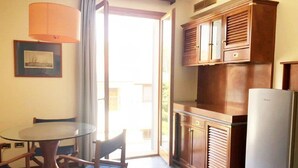 A kitchen with a dining table and chairs, wooden cabinets, a refrigerator, and a window with curtains. - Zì Maria (Cecina)