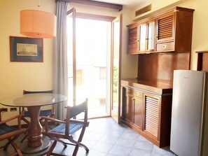 A kitchen with a dining table and chairs, wooden cabinets, a refrigerator, and a window with curtains. - Zì Maria (Cecina)