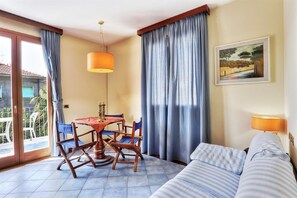 A room with a dining table, chairs, a sofa, a painting, and a view through a glass door.