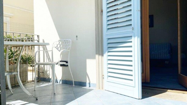 A patio area with a white metal table and chairs, a white door with horizontal louvered shutters, and a tiled floor. - Zì Maria (Cecina)