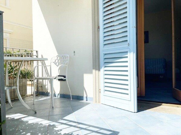 A patio area with a white metal table and chairs, a white door with horizontal louvered shutters, and a tiled floor.