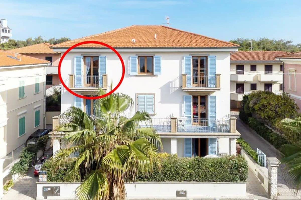Un bâtiment à deux étages, avec un toit recouvert de tuiles rouges, des volets bleus et un balcon.