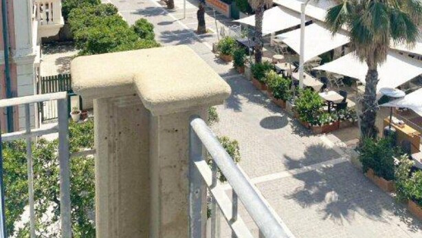 Une rue côtière bordée de palmiers et de bâtiments aux toits recouverts de tuiles rouges.