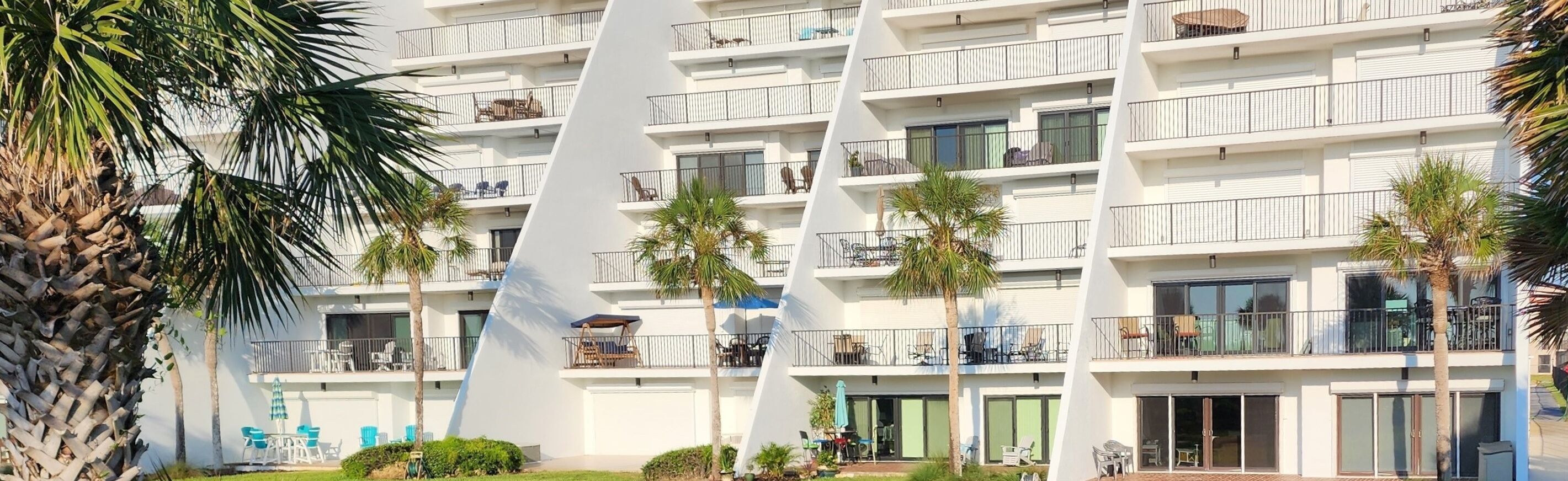 A multi-story hotel with balconies, outdoor seating, and palm trees.