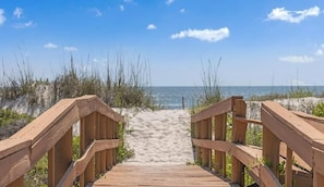 A wooden boardwalk leading to a sandy beach with the ocean in the background.