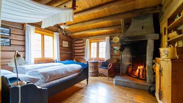 A log cabin room with a bed, a fireplace, and a wicker chair. - Roisheim (Lom)