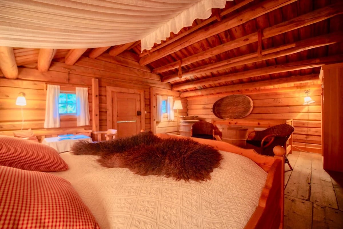 A log cabin room with a large bed, a wooden ceiling, and a rustic ambiance.
