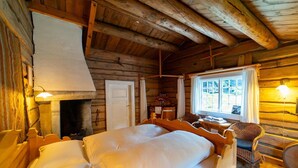 A cozy log cabin bedroom with a large bed, a fireplace, a window with curtains, and a wooden ceiling. - Roisheim (Lom)