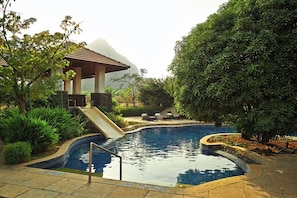 A swimming pool with a slide, surrounded by lush greenery and a gazebo. - Club Mahindra Resort - Tungi (Ootacamund)