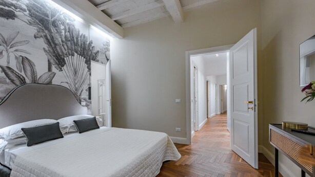Ein Schlafzimmer mit Bett, Kopfteil, einer Wand mit Pflanzenmotiv, Holzboden und einer Tür zu einem anderen Raum.
