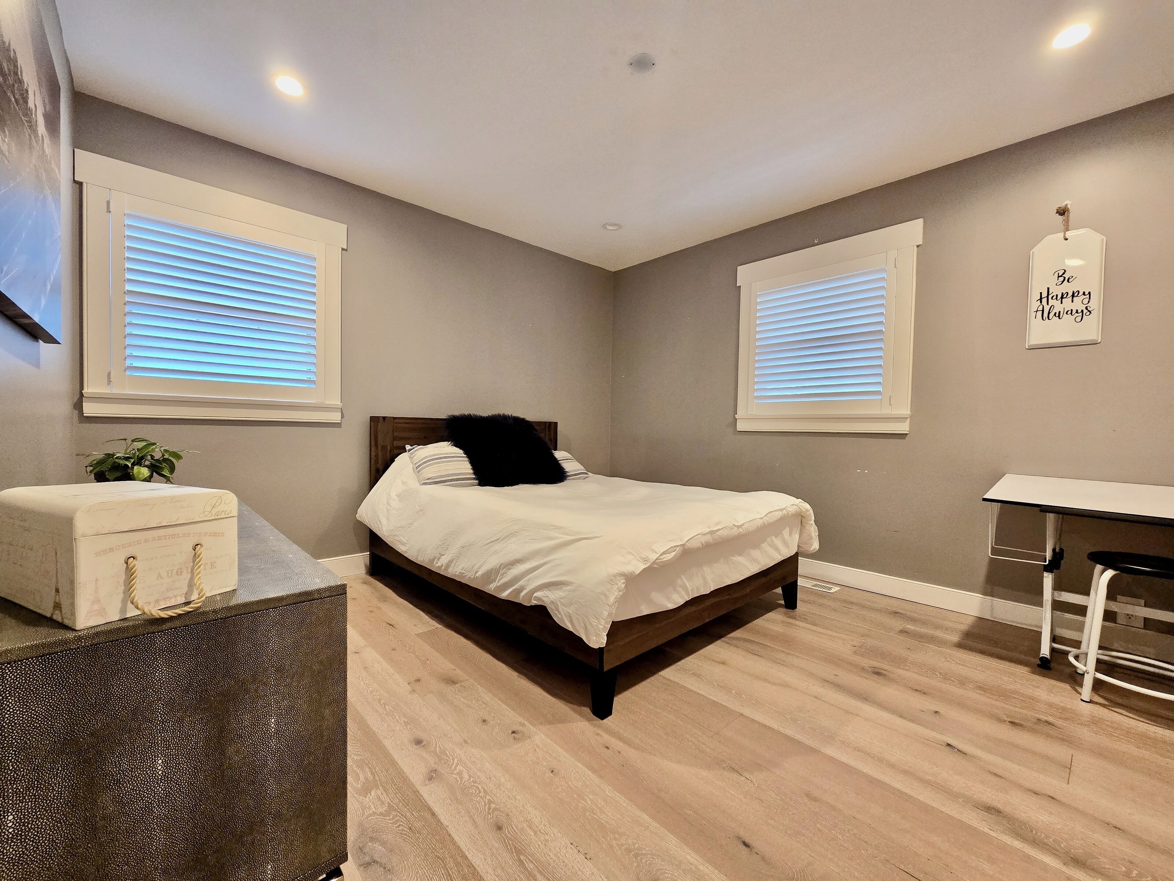 Un dormitorio con una cama, un escritorio y dos ventanas con persianas.